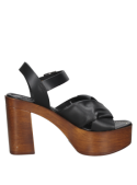 Calzado de cuero negro con tacón cuadrado y hebilla, evocando moda retro, ideal para eventos casuales al aire libre.