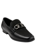 Detalle del zapato de cuero negro mostrando costuras definidas y cadena metálica que aporta un toque moderno.
