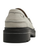 Mocasín beige de cuero para mujer con adorno metálico elegante y suela negra robusta.